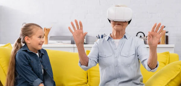 Niño positivo mirando a la abuela en auriculares de realidad virtual, pancarta - foto de stock
