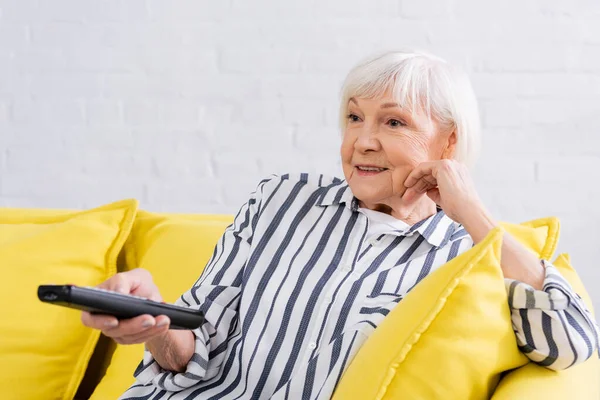 Heureuse femme âgée regardant un film sur le canapé — Photo de stock