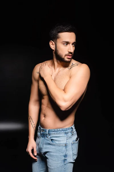 Muscular man in jeans looking away on black background — Stock Photo