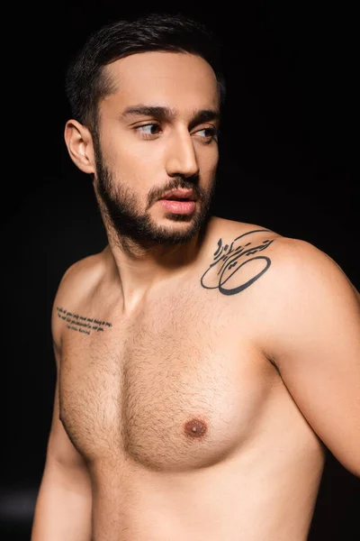 Hombre tatuado con torso sin camisa mirando hacia otro lado aislado en negro - foto de stock