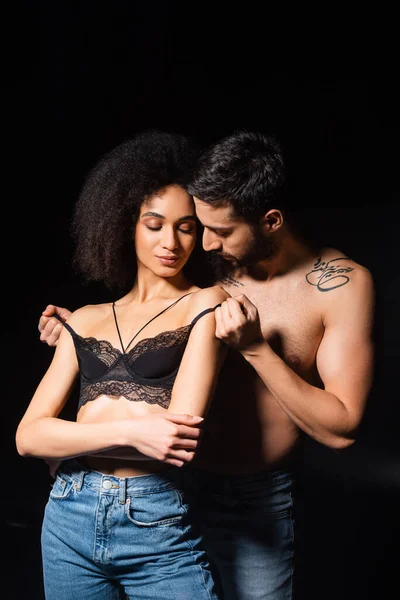 Hombre desvestirse seductora africana americana novia en sujetador aislado en negro - foto de stock