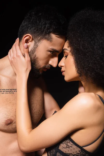 Vue latérale de la femme afro-américaine touchant torse nu petit ami isolé sur noir — Photo de stock