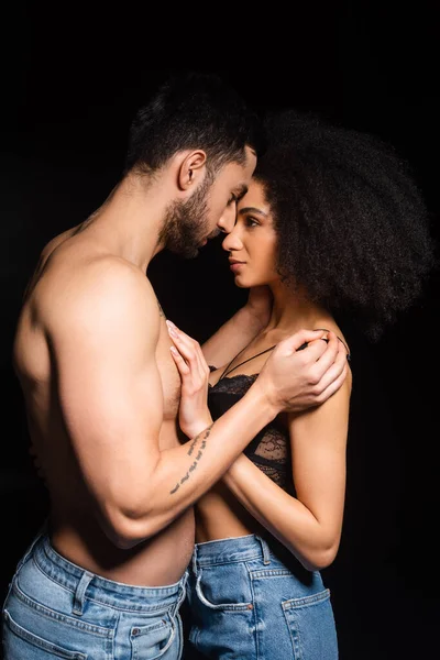 Vista laterale di uomo senza maglietta che abbraccia la ragazza afro-americana isolata sul nero — Foto stock