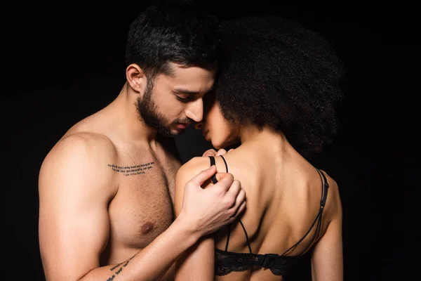 Hombre tatuado desnudando mujer afroamericana aislada en negro - foto de stock