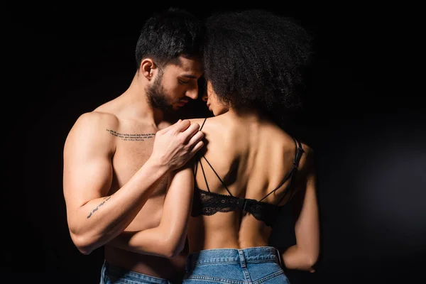 Afroamerikanerin im BH umarmt muskulösen Freund isoliert auf schwarz — Stockfoto