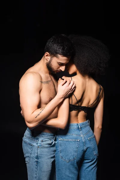 Міжрасові пари в джинсах обіймаються ізольовано на чорному — стокове фото