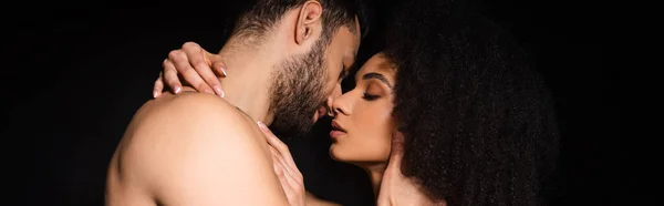 Vista laterale dell'uomo senza maglietta che bacia la ragazza afroamericana isolata sul nero, banner — Foto stock