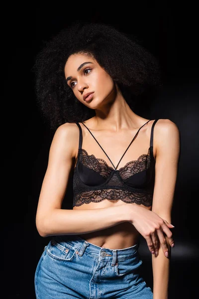 Pretty african american woman in bra touching arm on black background — Stock Photo