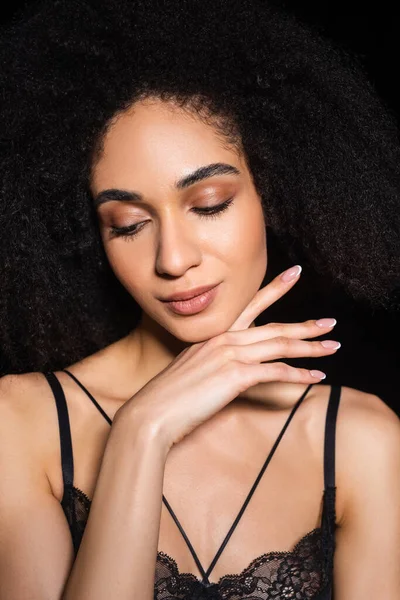 Young african american woman in bra holding hand near chin isolated on black — Stock Photo
