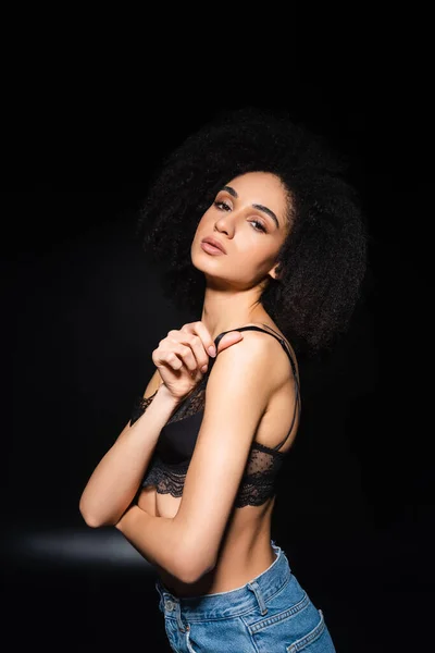 Jolie femme afro-américaine tenant une sangle de soutien-gorge sur fond noir — Photo de stock