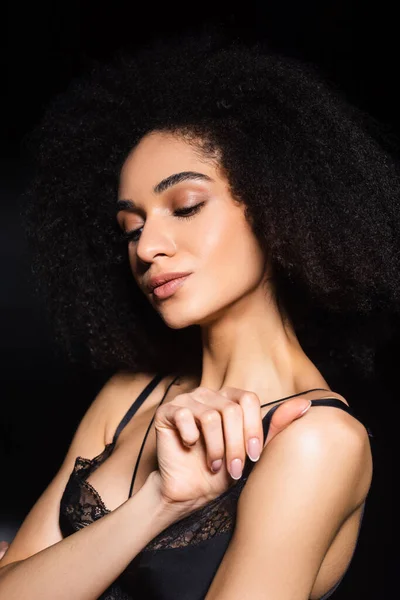 Спокуслива афроамериканська жінка тримає ремінь мереживного бюстгальтера ізольовано на чорному — стокове фото