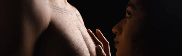 Side view of african american woman touching chest of boyfriend isolated on black, banner — Stock Photo