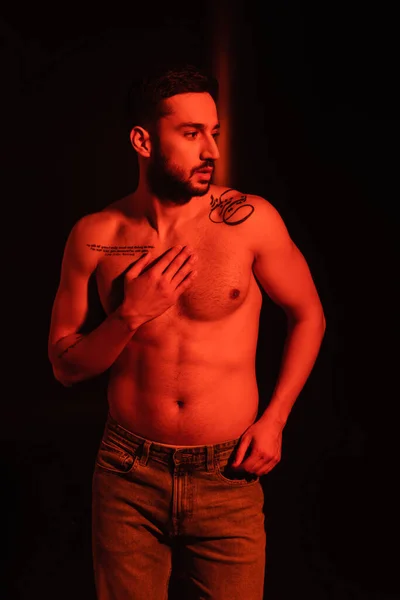 Muscular man touching chest on black background with red lighting — Stock Photo
