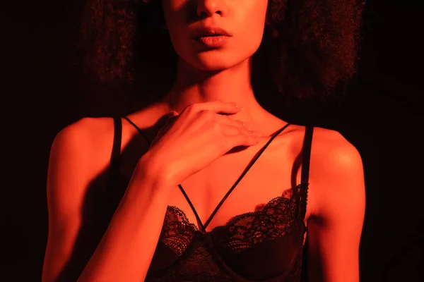 Cropped view of african american woman in bra touching neck isolated on black with red light — Stock Photo