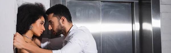 Side view of bearded man looking at pretty african american girlfriend near elevator, banner — Stock Photo