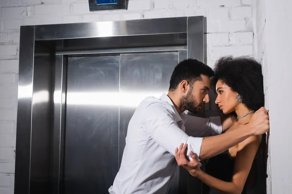 Vista lateral da mulher americana africana olhando para namorado barbudo na camisa perto do elevador — Fotografia de Stock