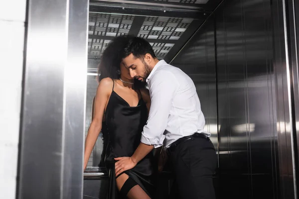 Hombre en ropa formal tocando novia afroamericana en ascensor - foto de stock