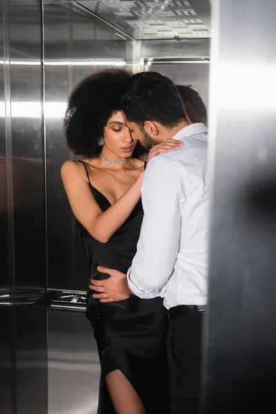 Afroamerikanerin im Kleid umarmt Freund im Fahrstuhl auf verschwommenem Vordergrund — Stockfoto