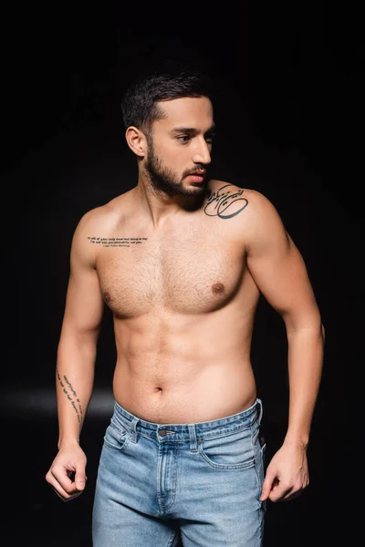 Hombre musculoso tatuado mirando hacia otro lado sobre fondo negro - foto de stock