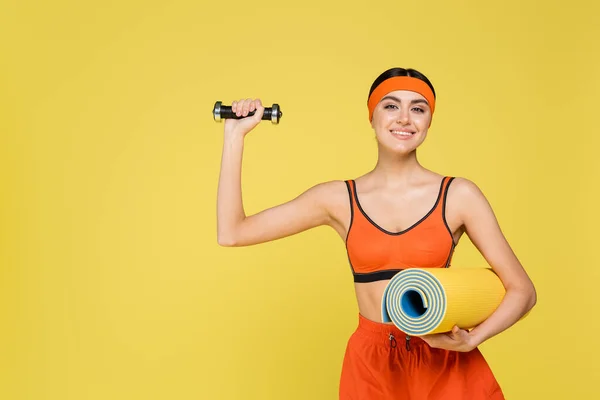 Молодая спортсменка с фитнес-коврик упражнения с гантели изолированы на желтый — стоковое фото