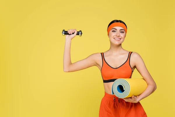 Jeune sportive avec tapis de fitness exercice avec haltère isolé sur jaune — Photo de stock