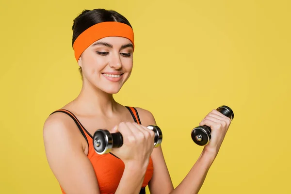 Zufriedene Sportlerin im orangefarbenen Top-Training mit auf Gelb isolierten Kurzhanteln — Stockfoto