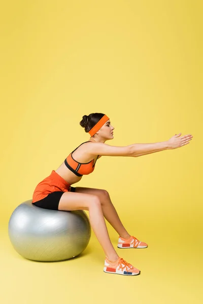 Junge Sportlerin in orangefarbener Sportbekleidung beim Training auf Fitnessball auf gelbem Hintergrund — Stockfoto