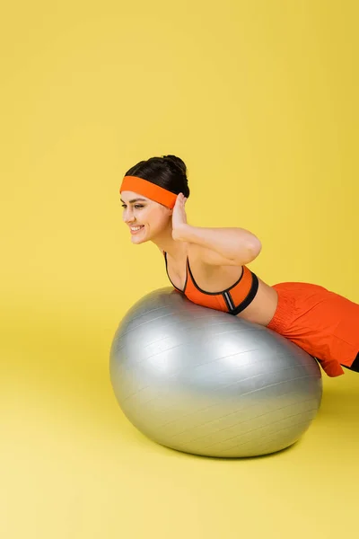 Smiling sportswoman exercitando na bola de fitness no fundo amarelo — Fotografia de Stock