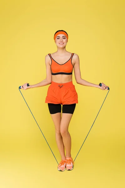 Щаслива спортивна жінка тренується зі стрибковою мотузкою ізольована на жовтому — стокове фото