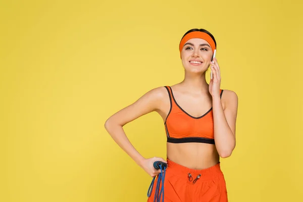 Cheerful sportswoman with jump rope talking on mobile phone isolated on yellow - foto de stock