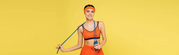 Joyful sportswoman with skipping rope smiling at camera isolated on yellow, banner — Stock Photo