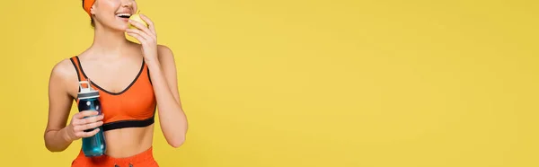 Cropped view of woman with sports bottle eating fresh apple isolated on yellow, banner — Stock Photo