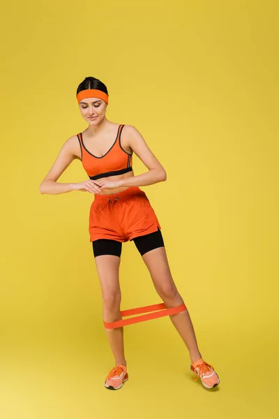 Jovem mulher esportiva trabalhando com elásticos no fundo amarelo — Fotografia de Stock