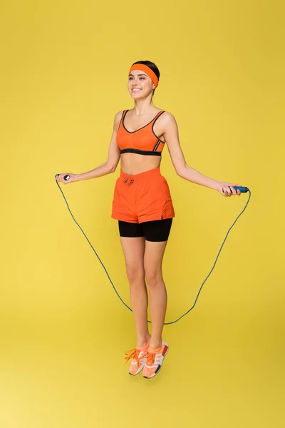 Happy sportswoman jumping with skipping rope isolated on yellow — Stock Photo