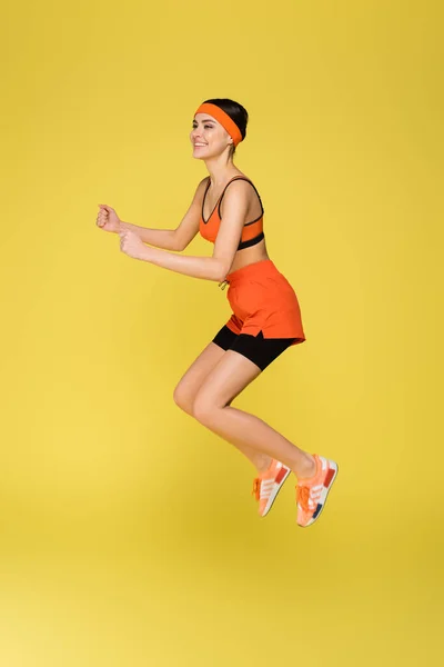 Cheerful woman in orange sportswear jumping isolated on yellow — Stock Photo