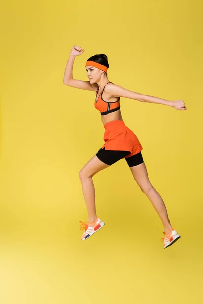 Visão de comprimento total da mulher esportiva correndo isolado no amarelo — Fotografia de Stock