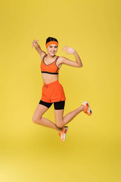 Excited sportswoman smiling at camera while jumping isolated on yellow — Stock Photo