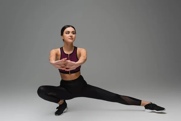 Jeune femme en tenue de sport noire s'étirant sur fond gris — Photo de stock