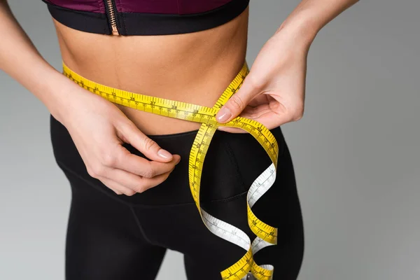 Partial view of sportswoman measuring waist isolated on grey — Stock Photo