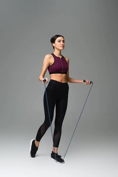 Vue pleine longueur de la femme en tenue de sport noire avec corde à sauter sur fond gris — Photo de stock