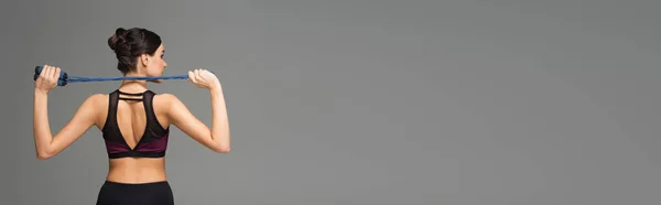 Vue arrière de jeune femme en tenue de sport noire tenant une corde à sauter isolée sur gris, bannière — Photo de stock