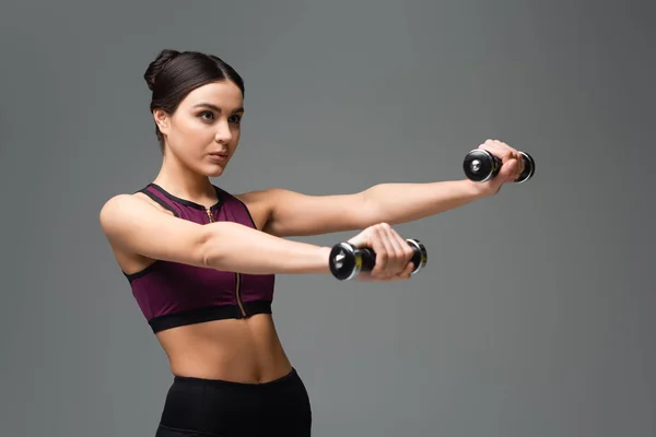 Confident sportswoman working out with dumbbells isolated on grey — Stock Photo