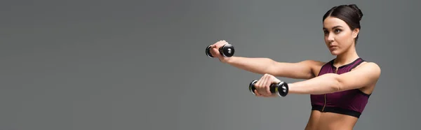 Young woman in black sports bra exercising with dumbbells isolated on grey, banner — Stock Photo