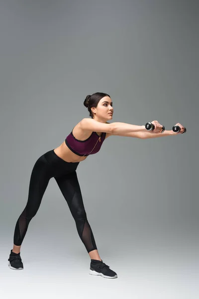 Sportswoman doing forward bends with dumbbells on grey background — Stock Photo