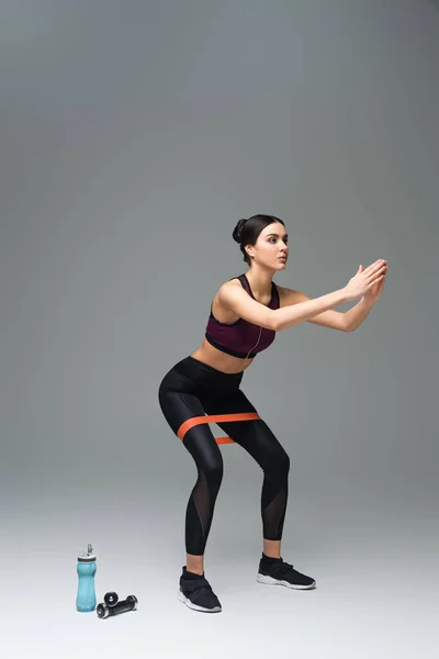 Sportswoman doing sit ups with resistance band on grey background — Stock Photo