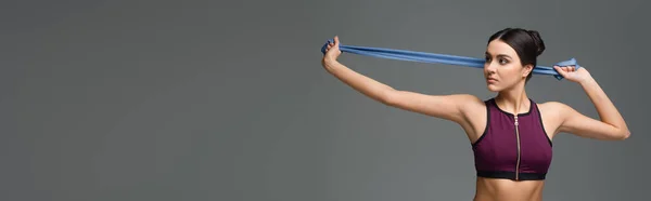 Bella donna in reggiseno sportivo nero che lavora con elastici isolati sul grigio, banner — Foto stock