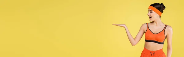 Erstaunt sportliche Frau steht mit offener Handfläche auf gelbem Banner — Stockfoto