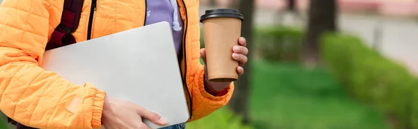 Vue recadrée de la femme tenant ordinateur portable et tasse en papier à l'extérieur, bannière — Photo de stock