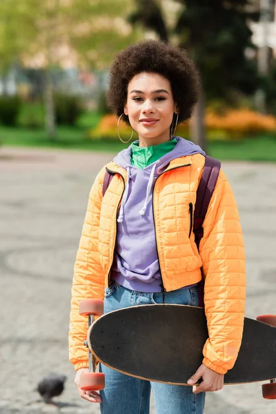 Sourire femme afro-américaine tenant longboard à l'extérieur — Photo de stock