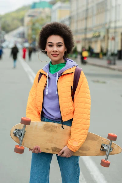 African american woman holding longboard on urban street — Stock Photo